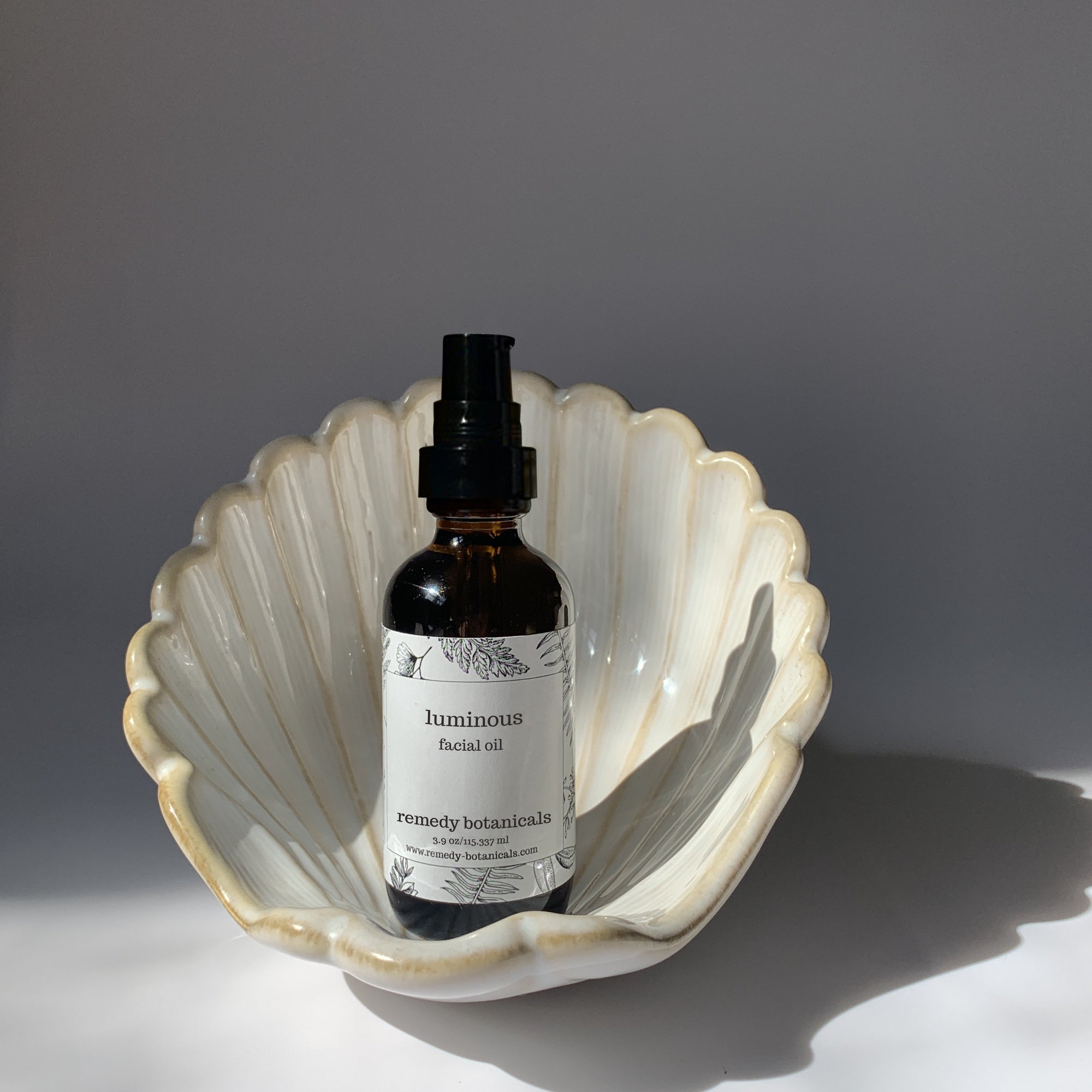 An luminous facial oil, standing on a pearl figurine on a gray blackground.